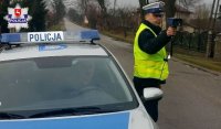 policjant dokonujący pomiaru prędkości stojący obok policyjnego radiowozu