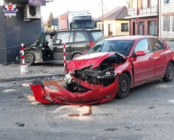 dwa rozbite samochody osobowe jeden stojący na ulicy drugi na chodniku