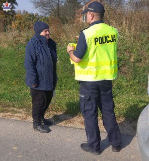 Policjant przekazuje kamizelkę odblaskową pieszej