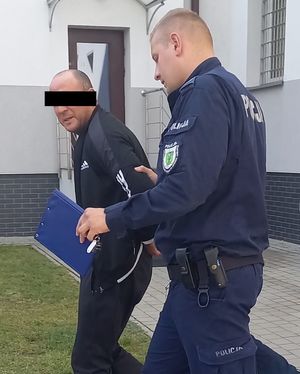 policjant prowadzi do radiowozu zatrzymanego mężczyznę