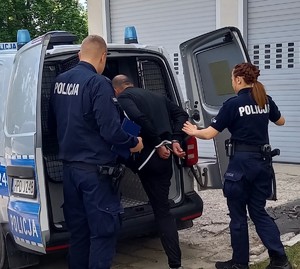 policjant i policjantka prowadzą do radiowozu zatrzymanego mężcyznę