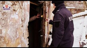 policjant stoi przy uchylonych drzwiach budynku