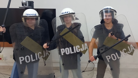 młodzież ubrana w policyjny sprzęt, kaski, pałki tarcze