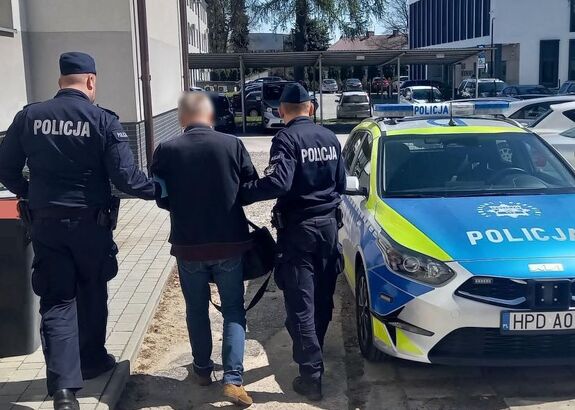 dwaj policjanci prowadzą zatrzymanego do samochodu