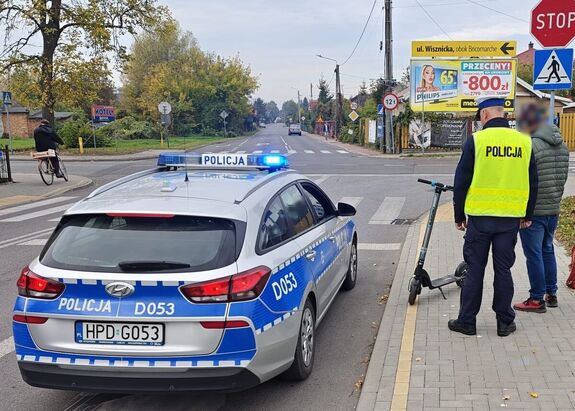 policjant i kierujący hulajnogą obok policyjny radiowóz